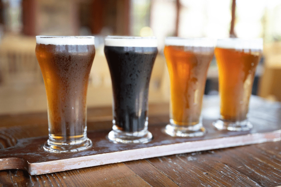 Tast de Cerveses 1 Cuatro vasos con cervezas de distintos estilos y colores en soporte de degustación sobre madera
