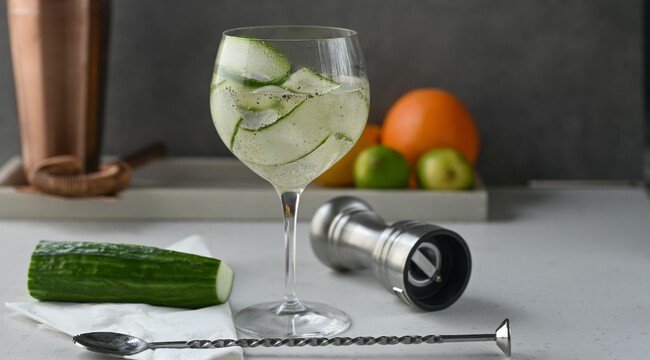 Copa balon de gin tonic con pepino, jigger y cuchara de bar sobre fondo neutro
