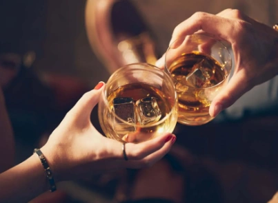 Dos personas brindando con vasos de whisky con hielo en cata a domicilio en Barcelona