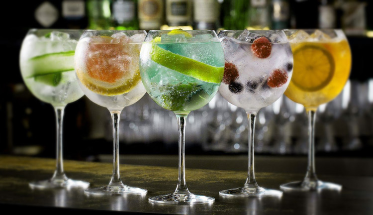 Cinco copas balloon de gin tonic con distintos botanicals y frutas sobre barra oscura