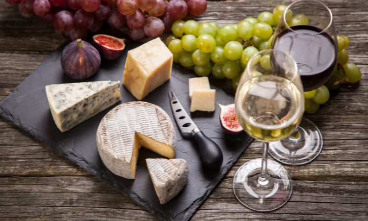Tabla de quesos con azul, brie y curado, uvas, higos y copas de vino blanco y tinto