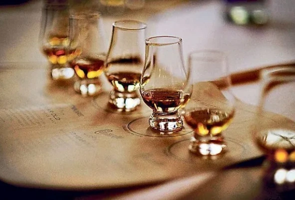 Cinco copas Glencairn con whiskies de distintas tonalidades sobre ficha de cata en taller
